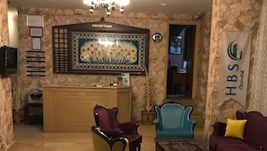 A reception area with a reception desk, a chandelier, and a reception sign. There are two armchairs and a blue chair in the seating area. - HBS Hotel (Kusadasi)