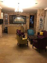 Un área de recepción con un mostrador, una araña y un letrero de recepción. Hay dos sillones y una silla azul en la zona de estar.