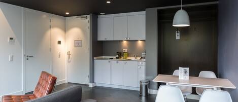 A modern kitchen with white cabinets, a dining area with a table and chairs, and a grey sofa.