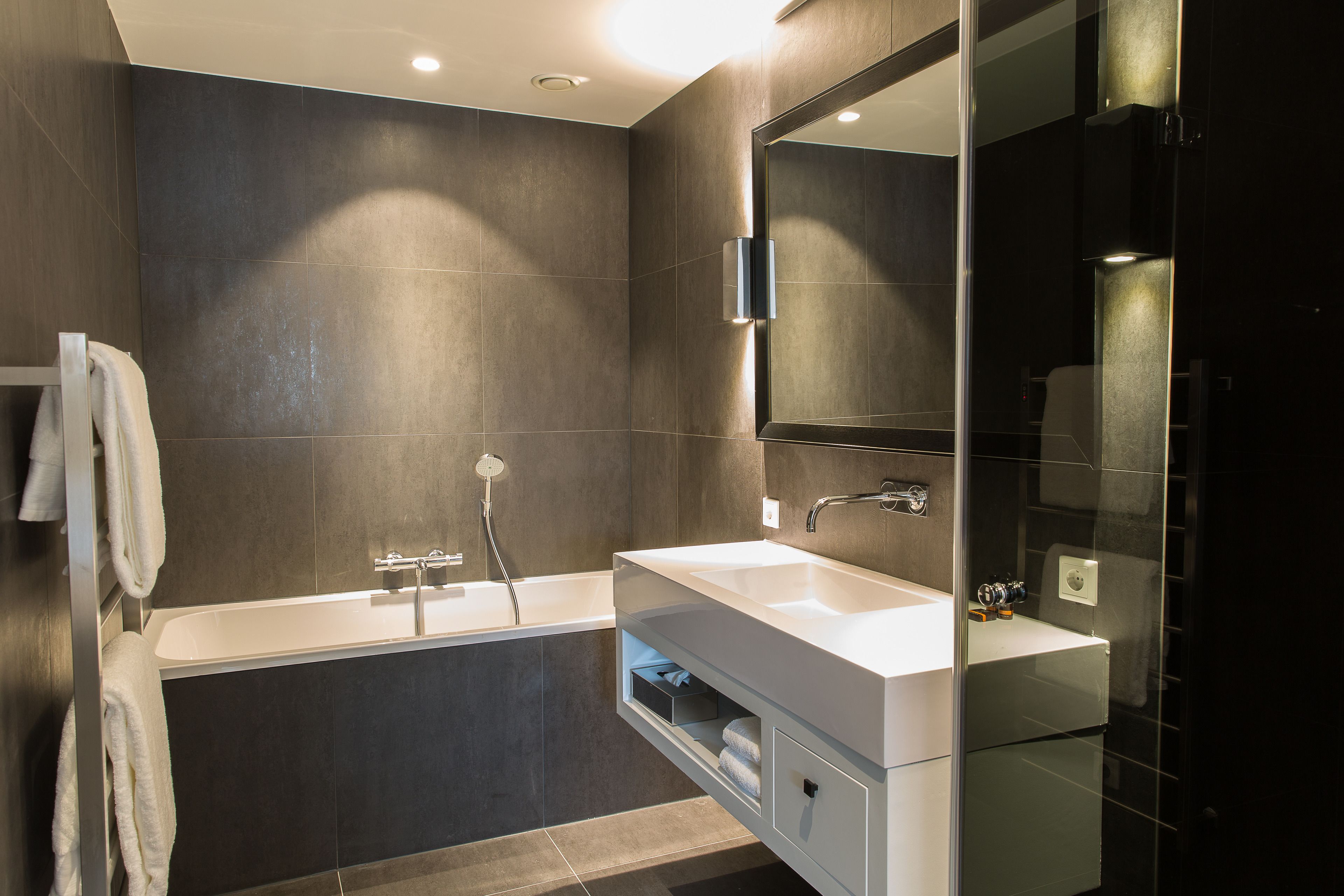 A modern bathroom with a bathtub, a large mirror, and a vanity with a sink.