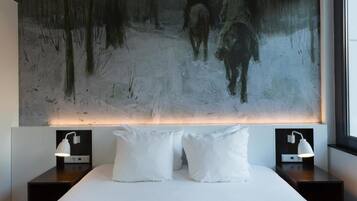 A modern hotel room with a large abstract painting on the wall, a neatly made bed with white linens, two bedside tables with lamps, and a window providing natural light.