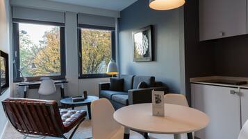 A modern room with a sofa, chairs, a table, and a view of autumn trees through large windows.