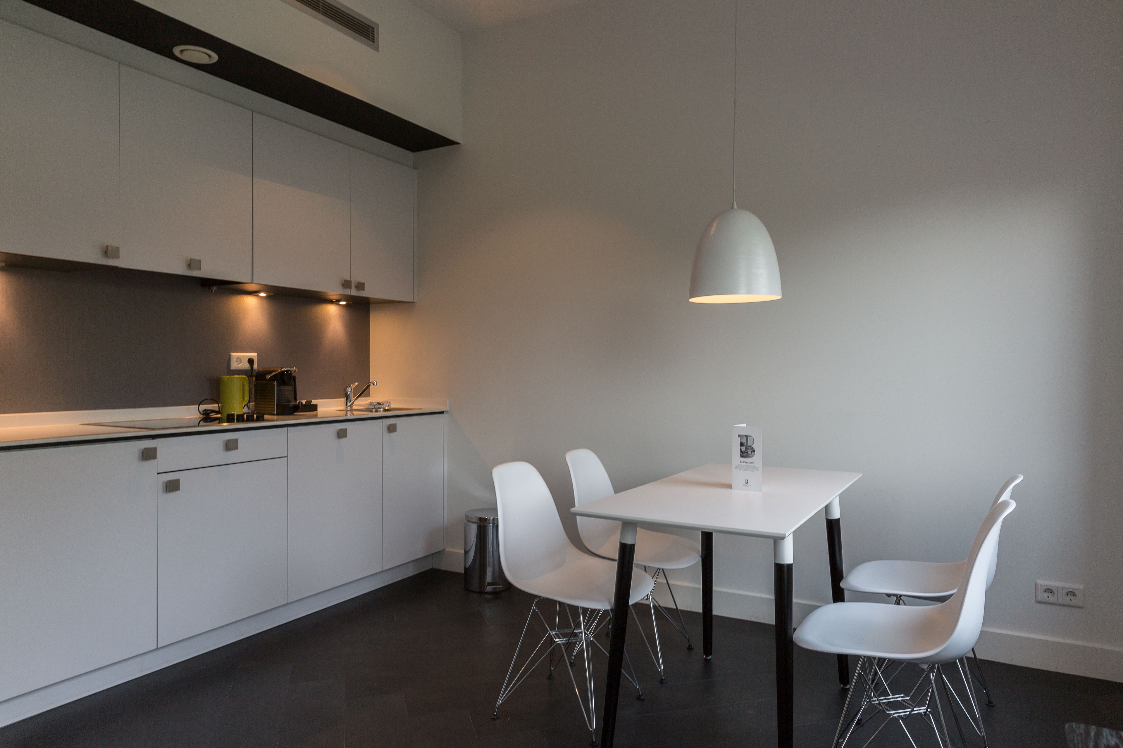 A modern kitchen with white cabinets, a white dining table, and four white chairs. There is a single pendant light above the table.