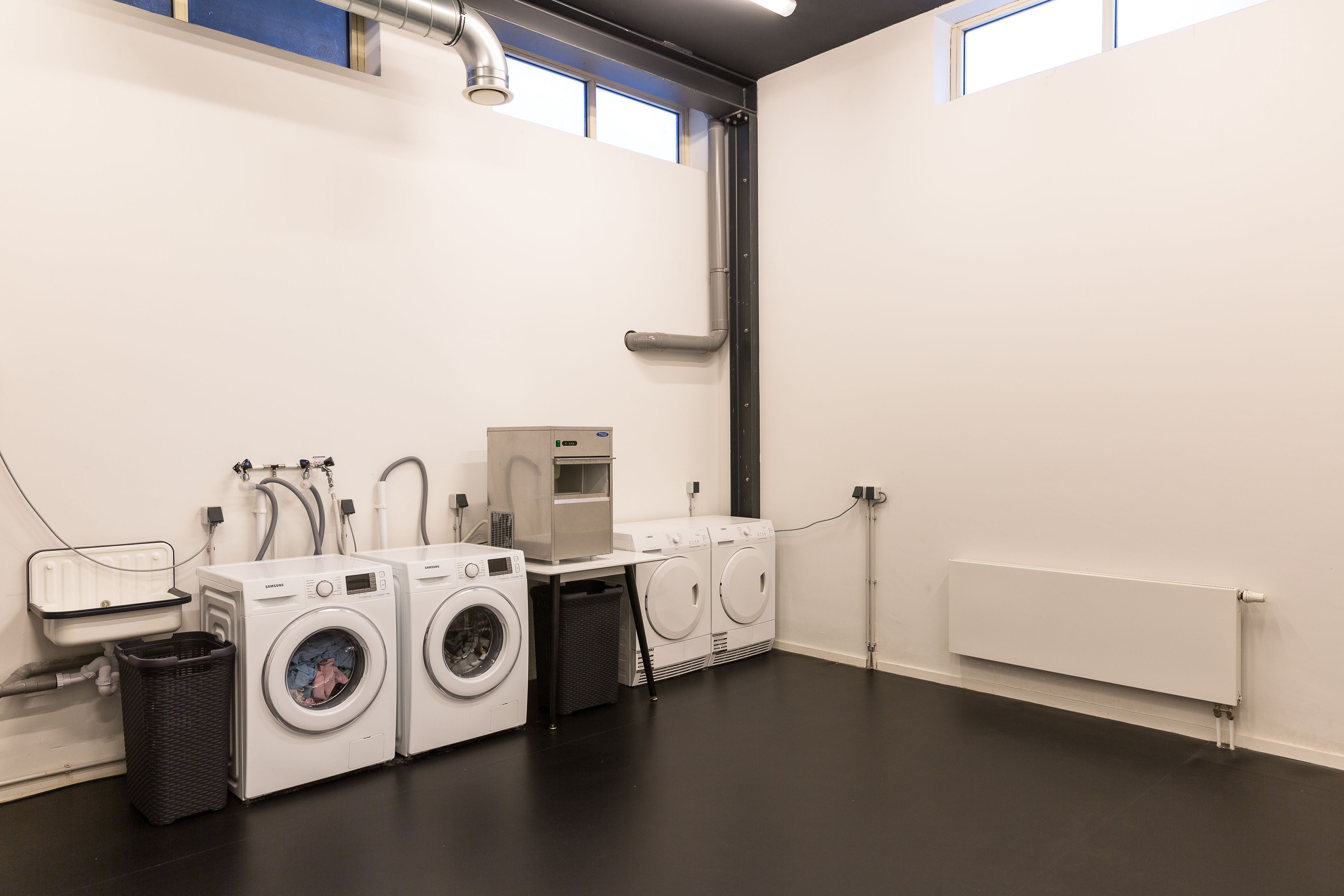 A laundry room with three washing machines, a dryer, and a water heater.