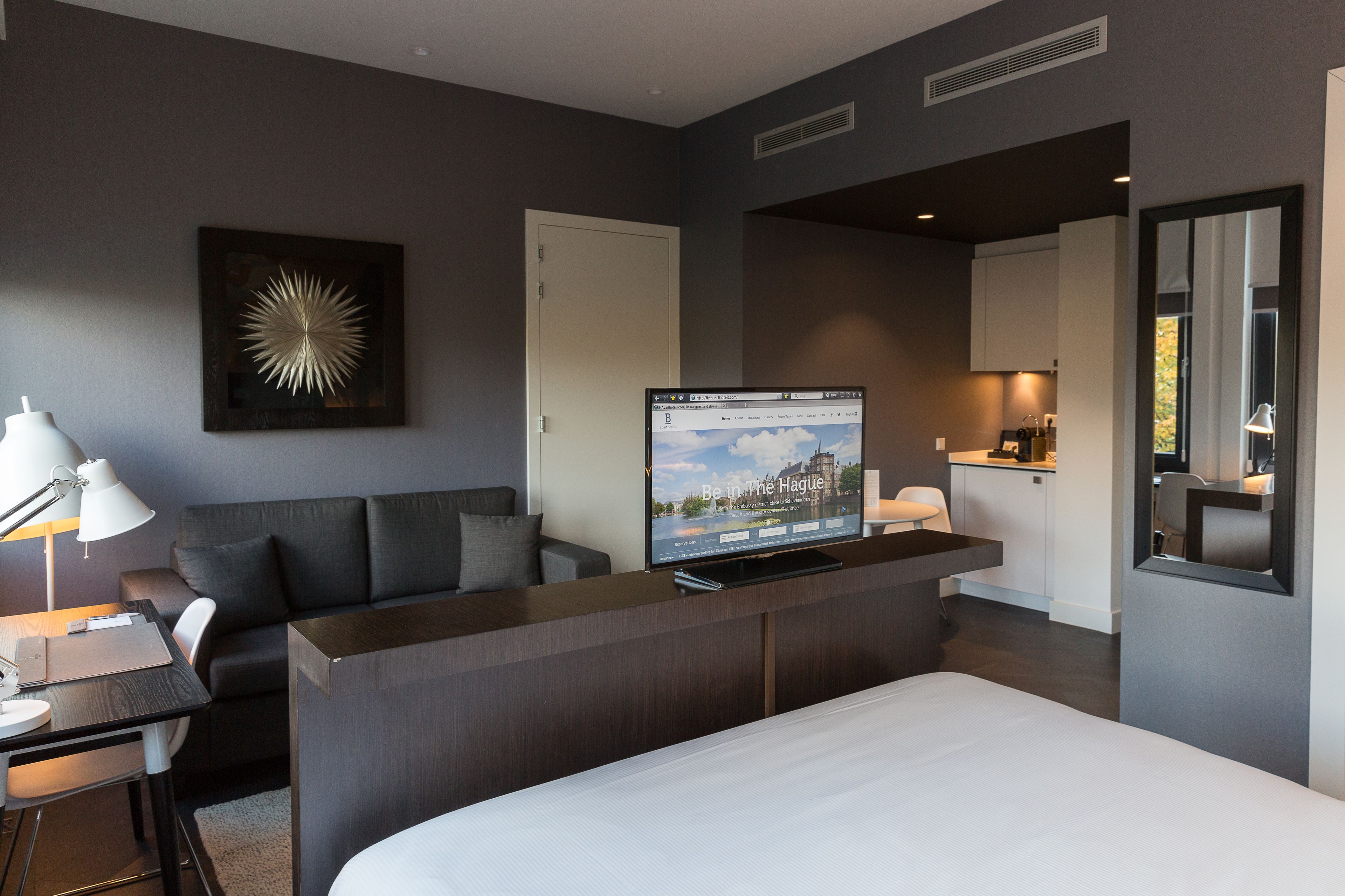 Een moderne hotelkamer met een bed, een bureau met een computer, een bank, een televisie en een badkamer.