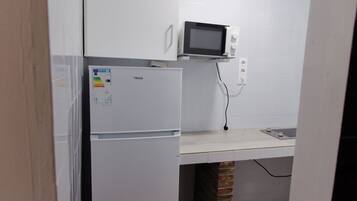 Una kitchenette compacta con un refrigerador blanco, un microondas y una pequeña encimera.