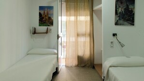 A hotel room with two single beds, a window with sheer curtains, and a wall-mounted lamp. - Hospedaje Lisboa Algeciras (Algeciras)