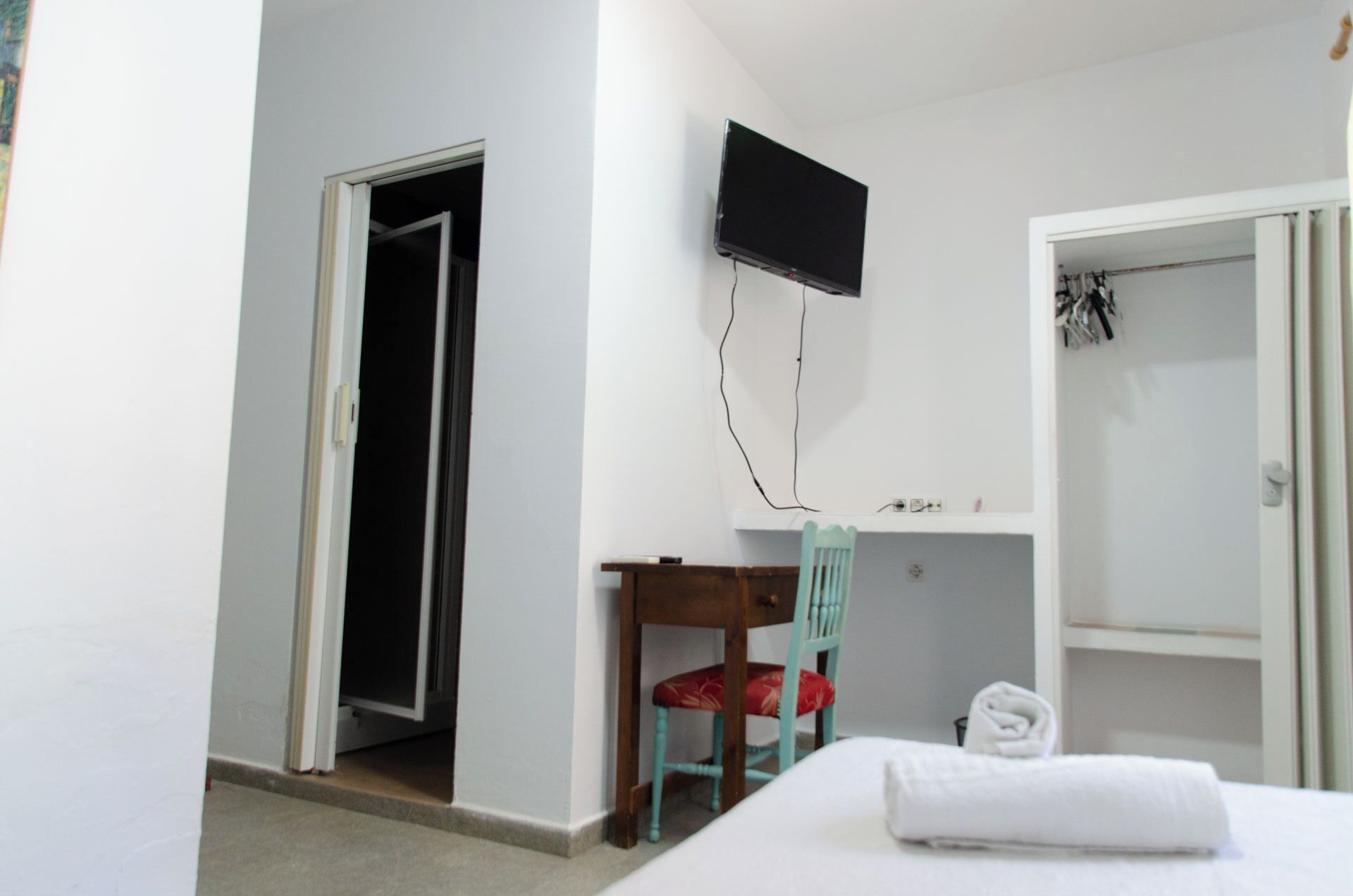 Habitación de hotel con cama, escritorio con silla, televisor montado en la pared y armario.