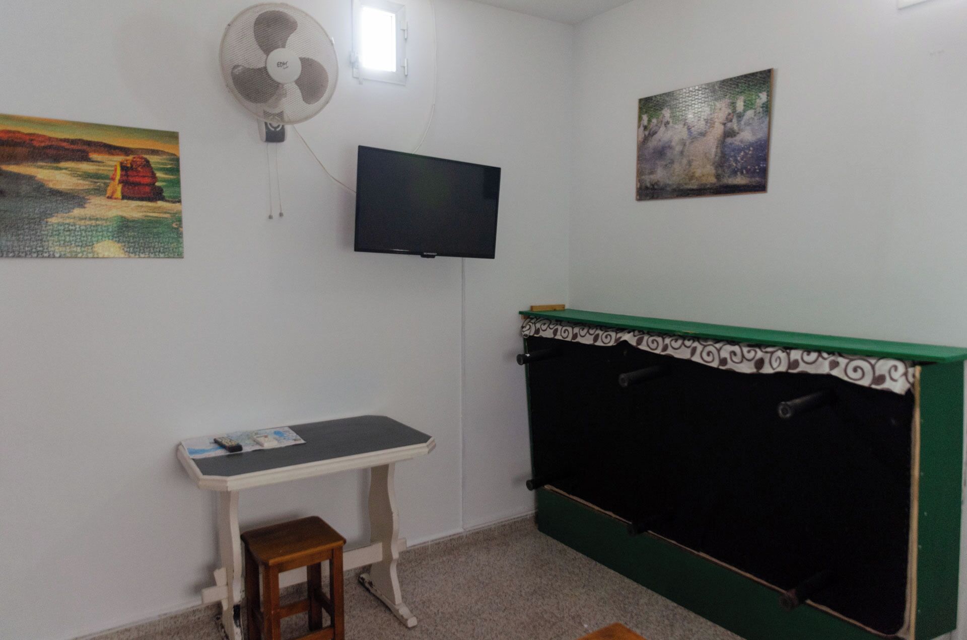 A room with a bed, a desk, a chair, a television, and two paintings on the wall.
