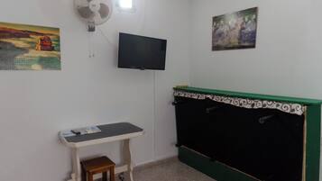 A room with a bed, a desk, a chair, a television, and two paintings on the wall.