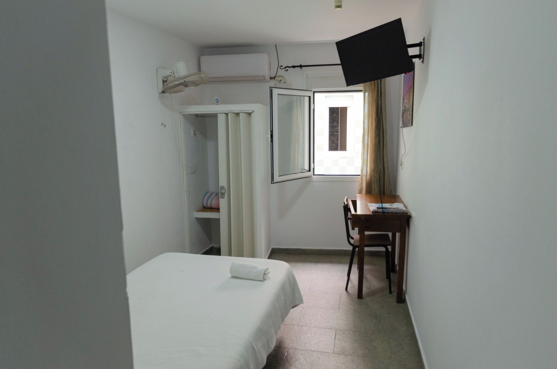 Una habitación pequeña y poco amueblada con una cama, un escritorio y una silla.