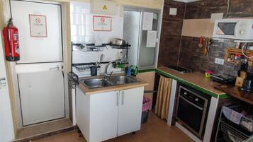 A compact kitchen with a sink, stove, and microwave. There are signs indicating no smoking and a fire extinguisher.