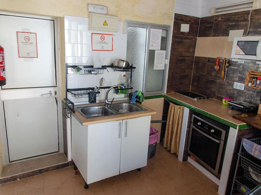 A compact kitchen with a sink, stove, and microwave. There are signs indicating no smoking and a fire extinguisher.