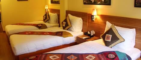 A hotel room with two beds, each with white linens and decorative pillows. There are wall-mounted lamps and framed artwork above the beds.