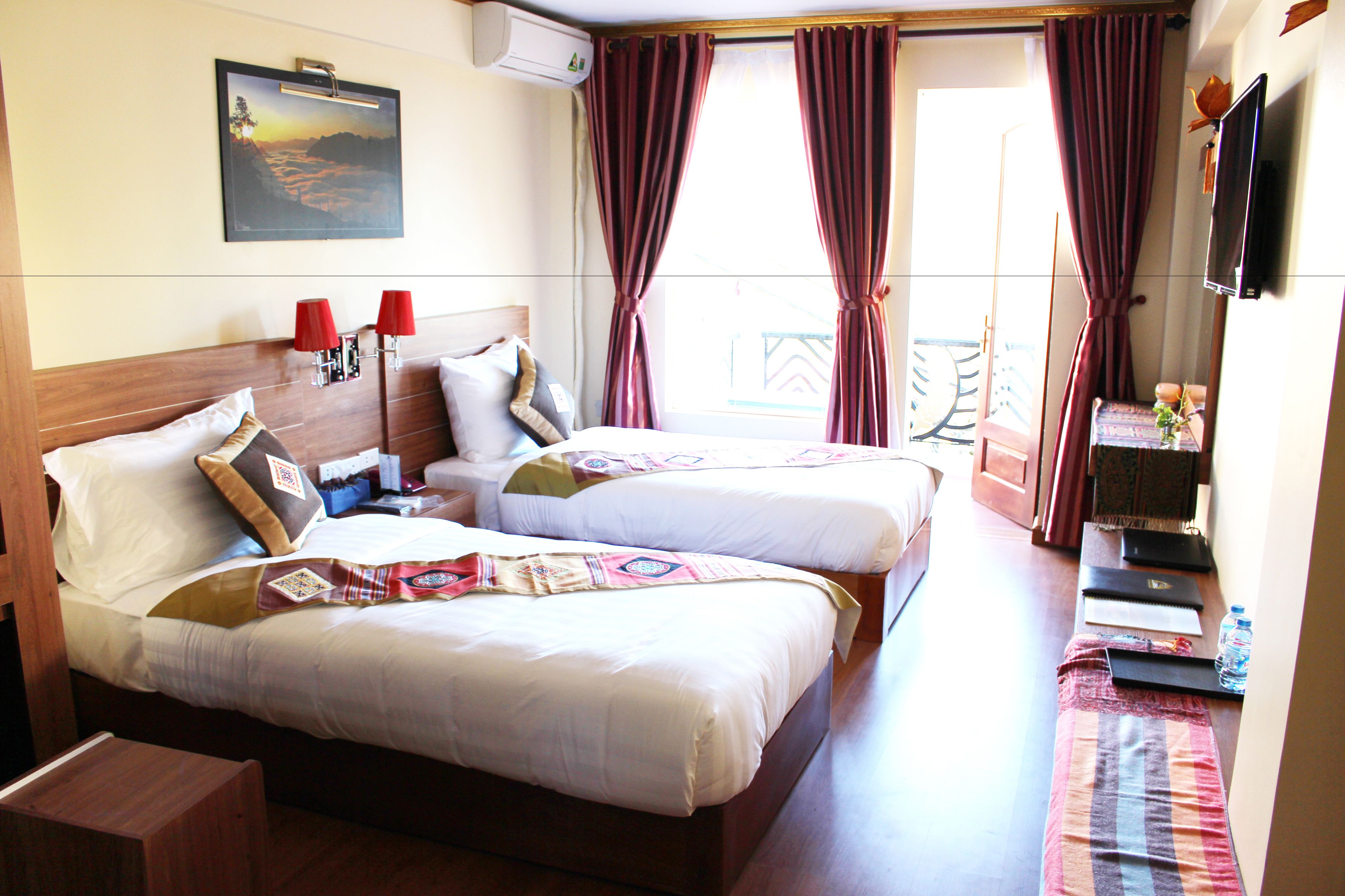 Habitación de hotel con dos camas, televisión, un cuadro y ventana con cortinas.