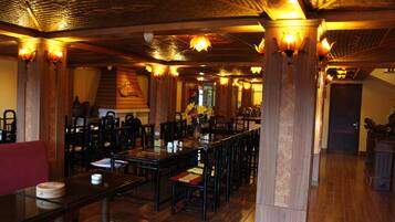 Un restaurante con mesas y sillas de madera, un sofá rojo e iluminación decorativa.