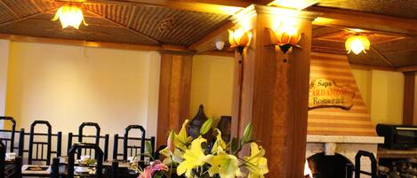 A restaurant interior with wooden ceiling, black chairs, and a table with flowers.
