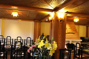 Interior de restaurante con techo de madera, sillas negras y una mesa con flores.