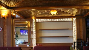 Interior de restaurante com design tradicional, apresentando parede estampada, teto de madeira e área de estar.