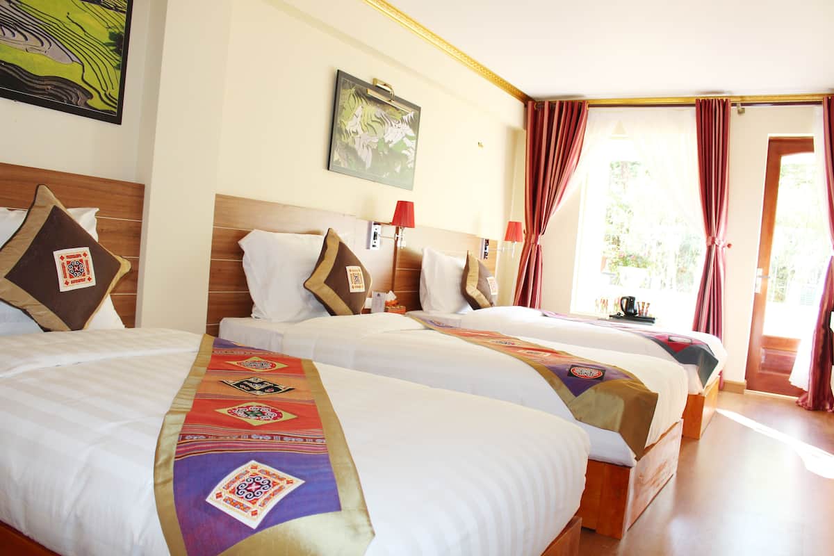 Habitación de hotel con dos camas, cada una con una colcha estampada, cabecero y mesita de noche con lámpara.