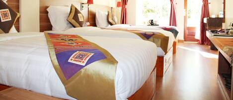 A hotel room with two beds, a wooden headboard, red curtains, a painting on the wall, and a desk with a chair.