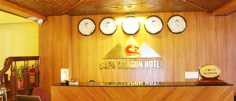 A reception desk with a wooden finish, a logo for Sapa Dragon Hotel, and four clocks on the wall.