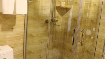 Cabina de ducha con paredes de vidrio, interior de madera, inodoro y un perchero con una toalla doblada.