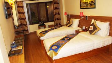 Quarto de hotel com duas camas, piso de madeira, uma janela grande com cortinas, uma obra de arte na parede e uma mesa de cabeceira com abajur.