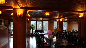 Um restaurante com mobiliário de madeira, janelas amplas e luminárias pendentes.