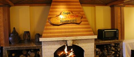 Ein Restaurantinneres mit Kamin, einem Schild mit der Aufschrift 'Sapa Cardamom Restaurant' und einem Fernseher auf einem Kaminvorsprung.