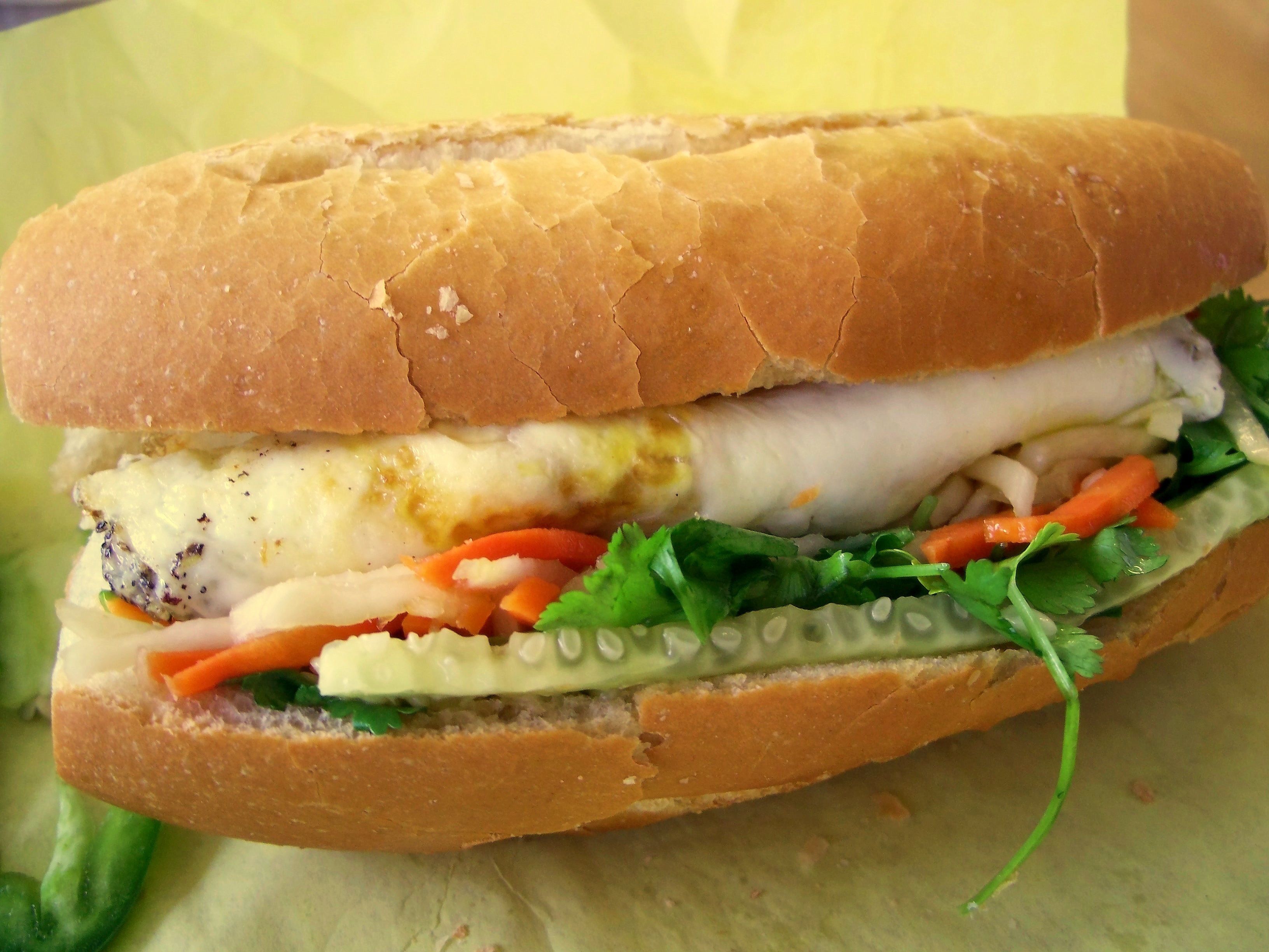 Un sándwich con pan crujiente, lechuga, tomate y un relleno blanco.