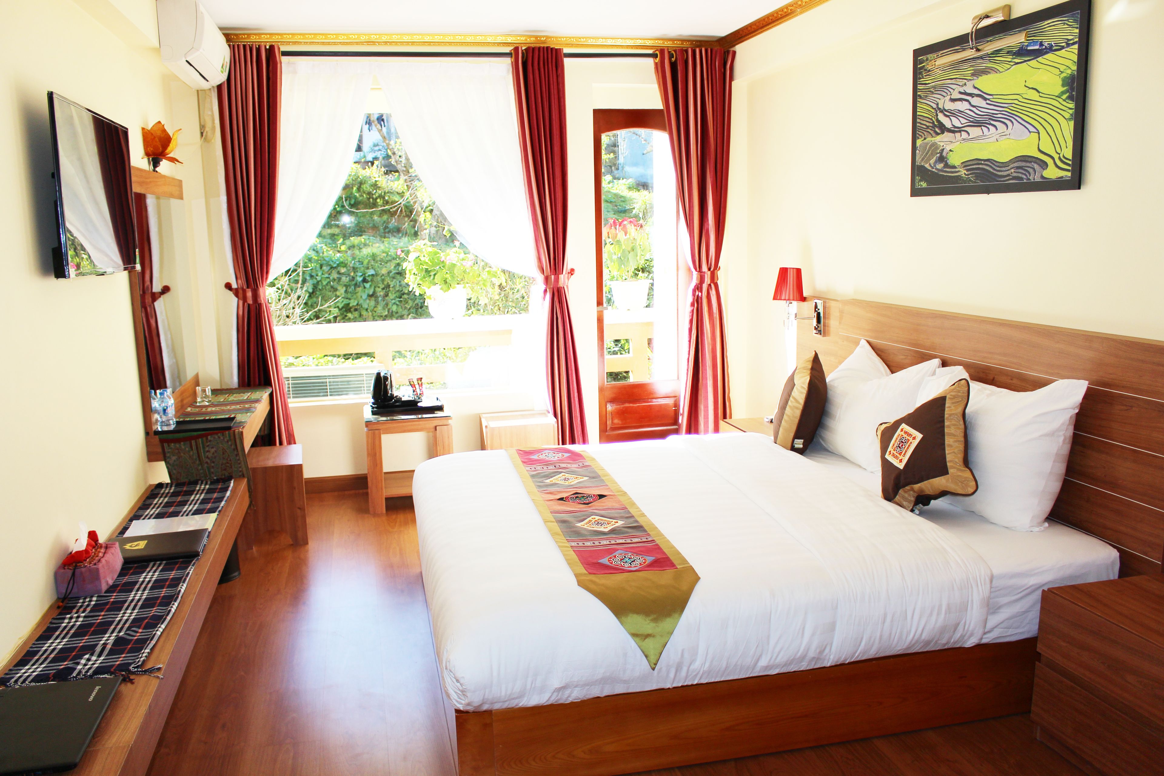 Een hotelkamer met een groot bed, een bureau met een laptop, een raam met gordijnen en een schilderij aan de muur.
