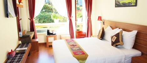 Een hotelkamer met een groot bed, een bureau met een laptop, een raam met gordijnen en een schilderij aan de muur.