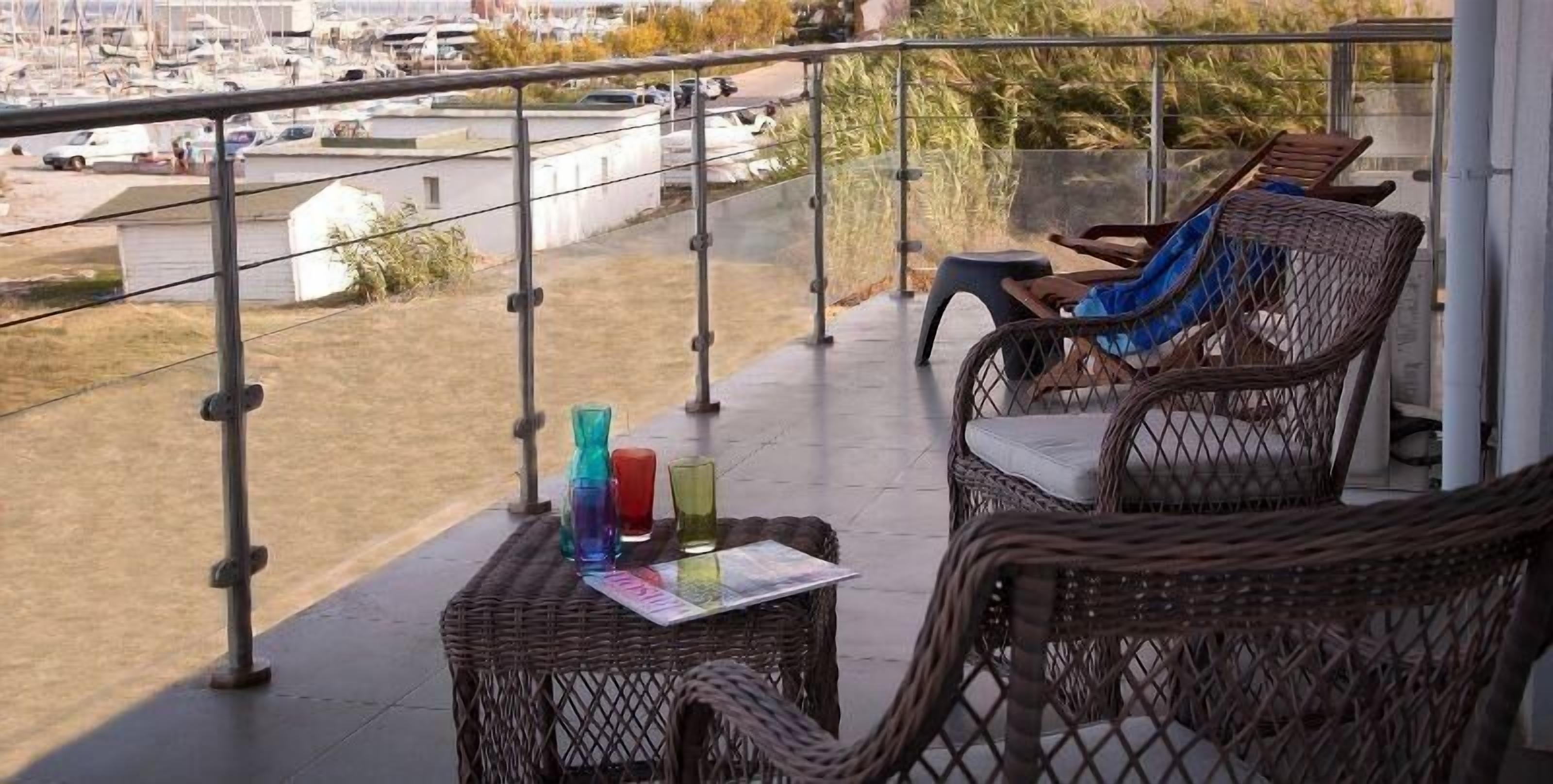 Un balcon agrémenté de meubles en osier, une petite table avec un magazine et des bouteilles en verre aux couleurs vives.