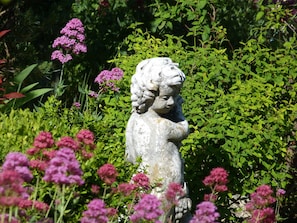 Una estatua en un jardín, rodeada de abundante vegetación y flores rosadas.