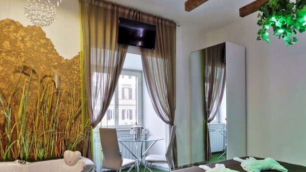 Camera d'albergo moderna con soffitto in legno, un letto grande, un angolo salotto con un tavolino e sedie, una vasca idromassaggio e vista sulla città attraverso ampie finestre.