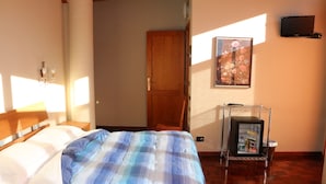 A bedroom with a bed, a nightstand, a wall-mounted TV, a door, and a small refrigerator. - Hotel Laghetto (Frabosa Sottana)