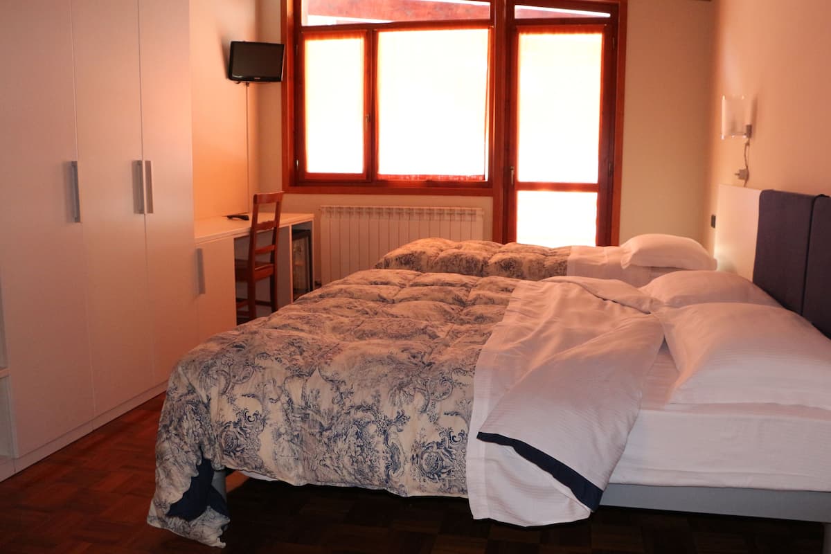 A bedroom with a bed, a desk, a chair, and a TV on the wall.