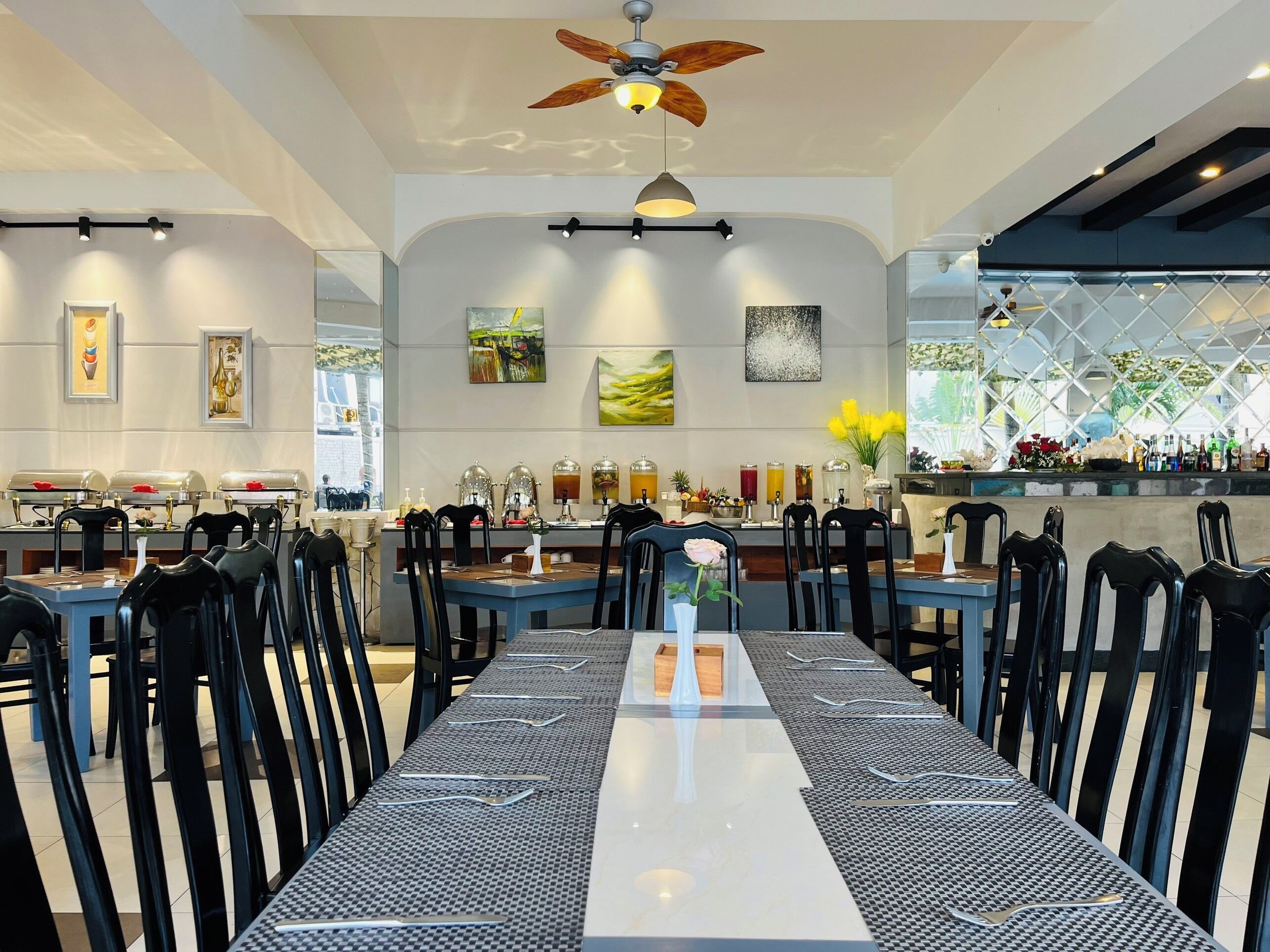 A restaurant with a long table, black chairs, and a ceiling fan.