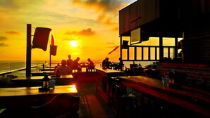 A sunset view from a restaurant with outdoor seating, a view of the sea, and a building with large windows. - Phu Quoc Ocean Pearl Hotel (Phu Quoc)