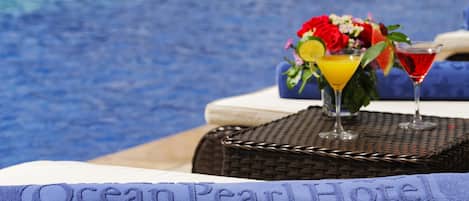 A hotel room with a bed, a wicker basket, and a table with a drink and flowers.