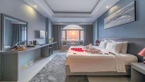A modern hotel room with a large bed, a desk, a mirror, and a view of the sunset through the window. - Phu Quoc Ocean Pearl Hotel (Phu Quoc)