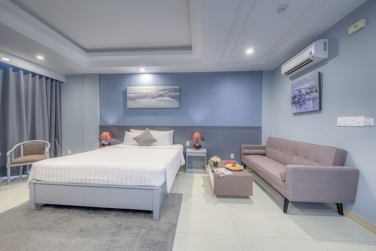 Un dormitorio moderno con cama, mesitas de noche, un sofá y un cuadro en la pared.