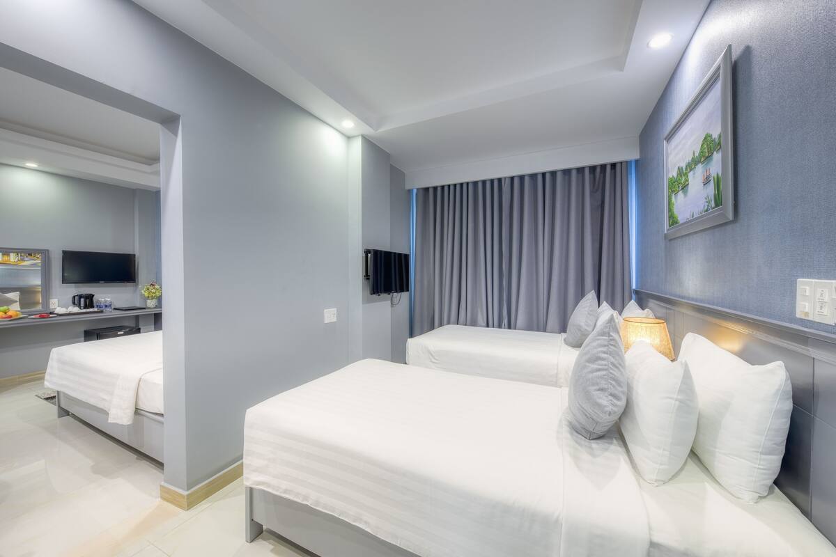 A hotel room with two beds, a TV, a desk with a coffee machine, and a painting on the wall.