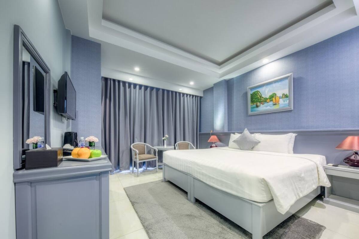 A modern hotel room with a large bed, a desk with a chair, a television, and a painting on the wall.