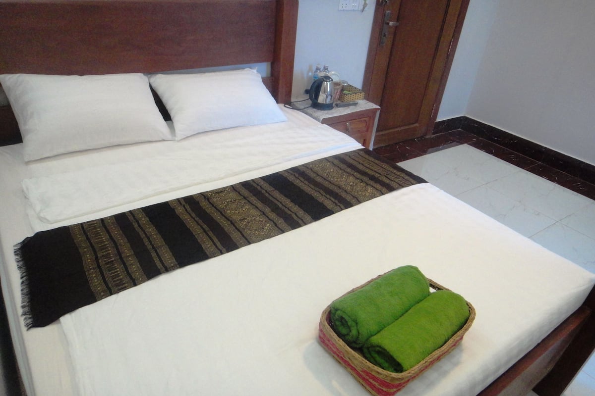 A neatly made bed with white linens, a striped blanket, and a green towel in a basket.