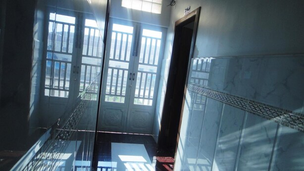 A corridor with a glass door leading to a balcony, a tiled wall, and a metal railing. - Marany Guesthouse (Kampot)