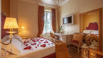A hotel room with a bed, a desk, a chair, a chandelier, and a large mirror.
