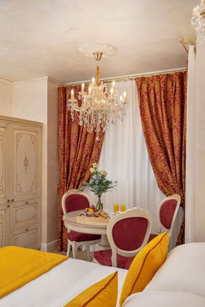 Una habitación de hotel con una cama, una mesa de comedor con sillas, un candelabro y cortinas.