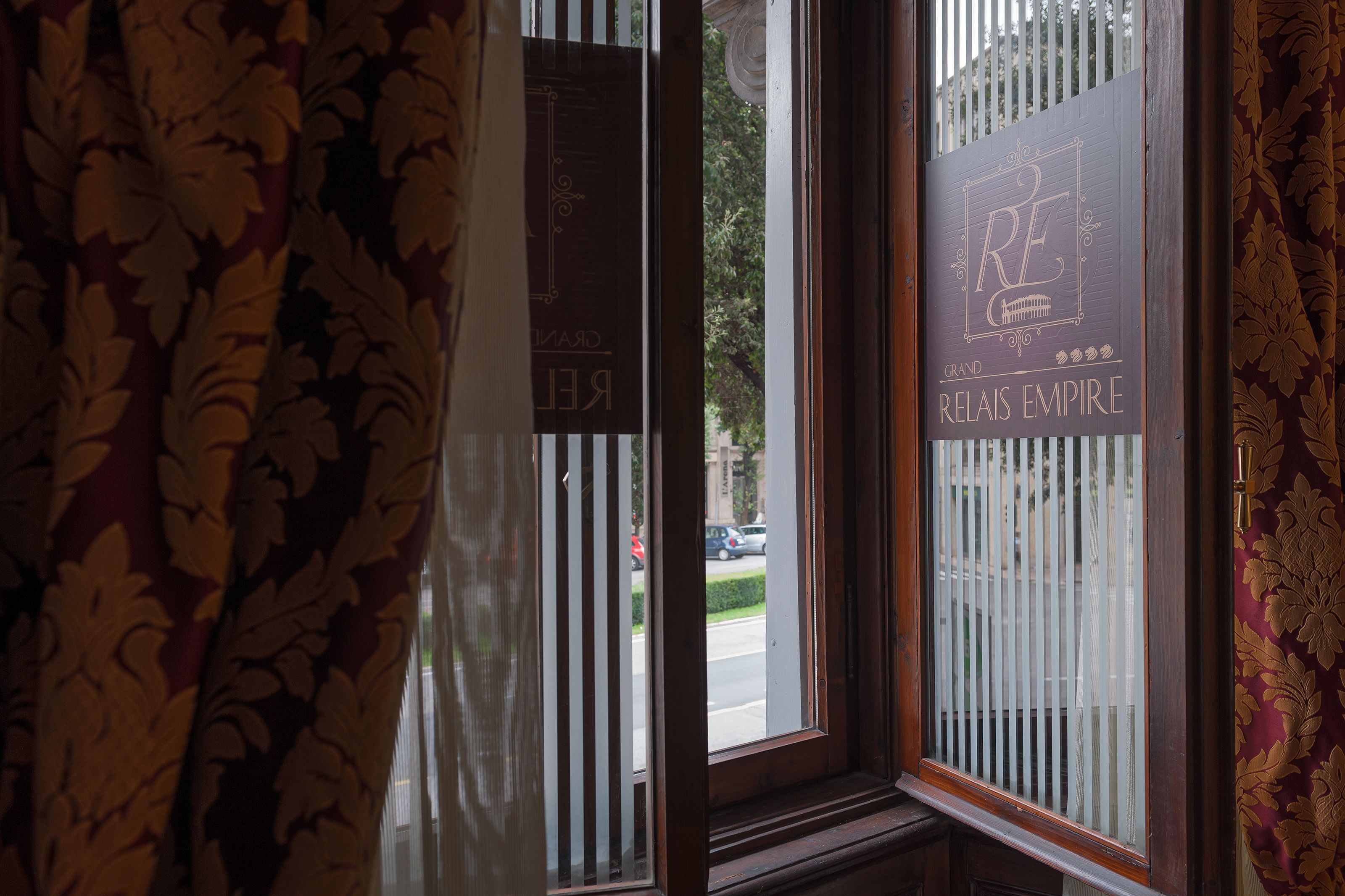 A window with vertical blinds and a sign that reads "Grand Relais Empire".